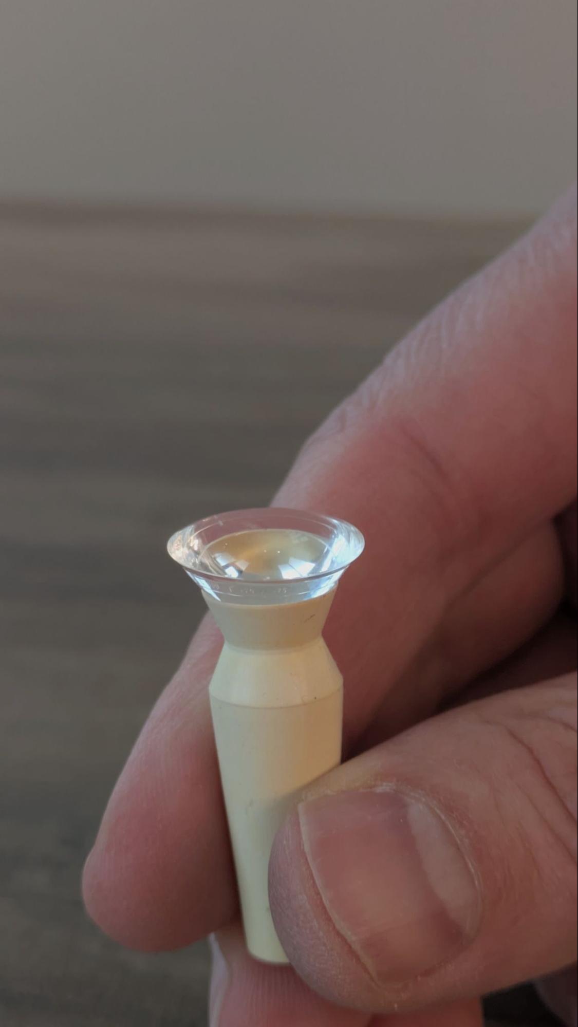 A hand holding a large scleral contact lens filled with solution on a beige insertion tool.